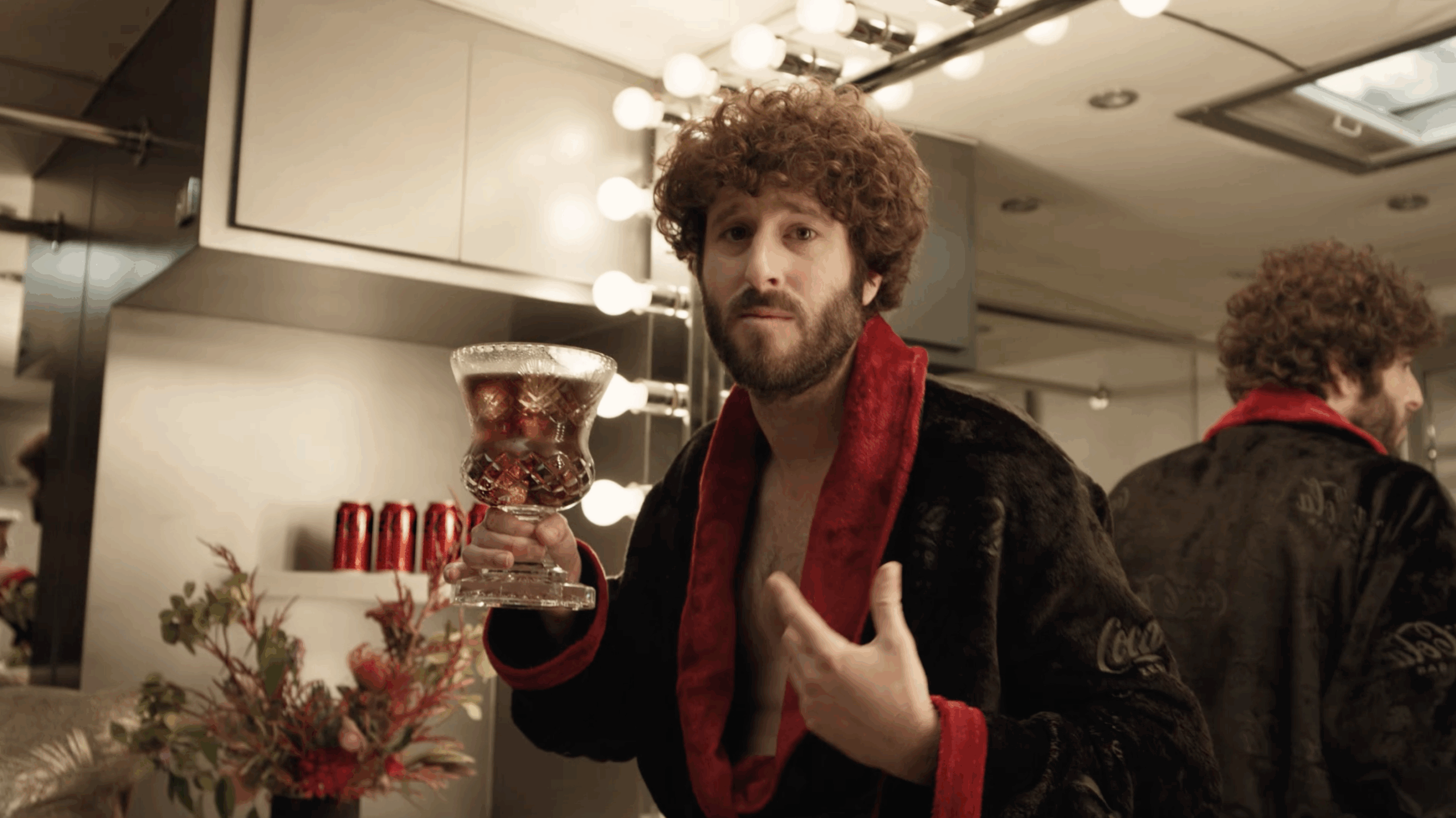 Screenshot from the "Debate the Goatness" ad campaign featuring Dave Burd wearing a Coca Cola branded robe colored black and red in a dressing room