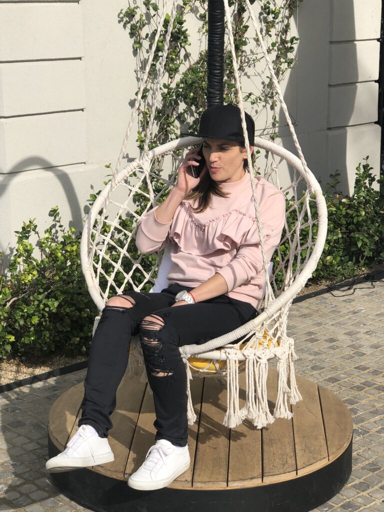 Photo of Deb sitting in a woven chair talking on the phone